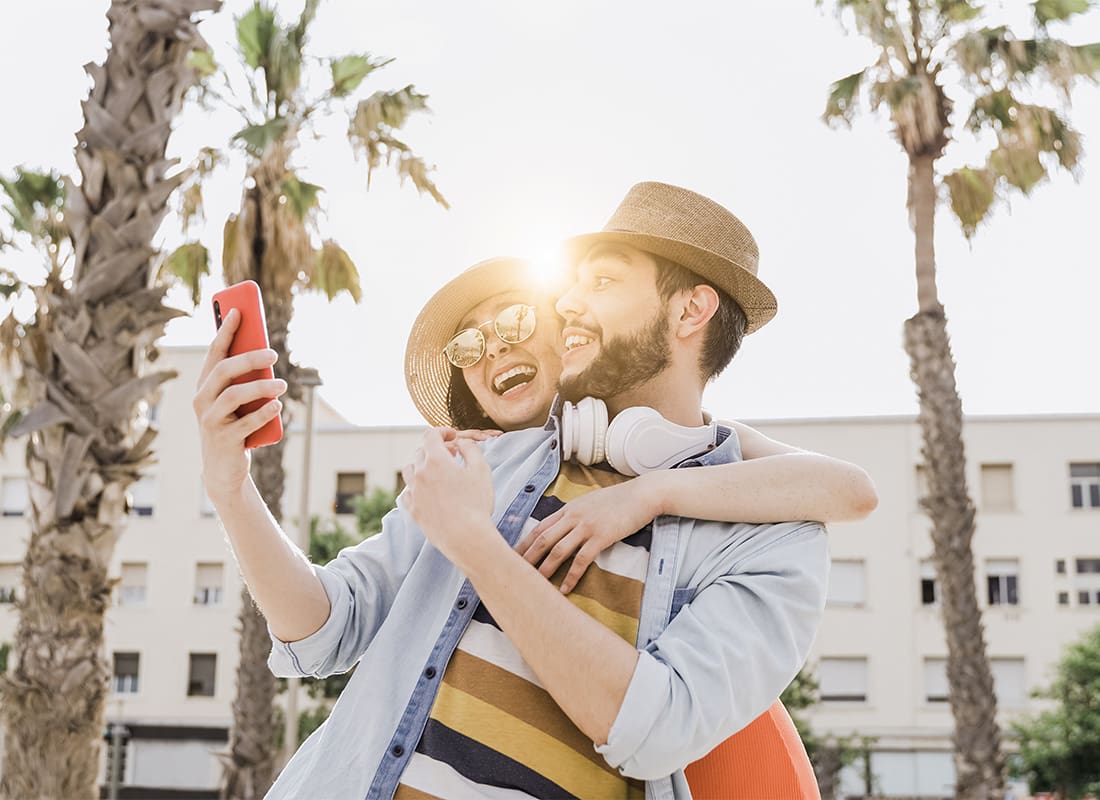 Read Our Reviews - Portrait of a Cheerful Young Couple Looking at a Phone While Standing Outside Next to Palm Trees on a Sunny Day